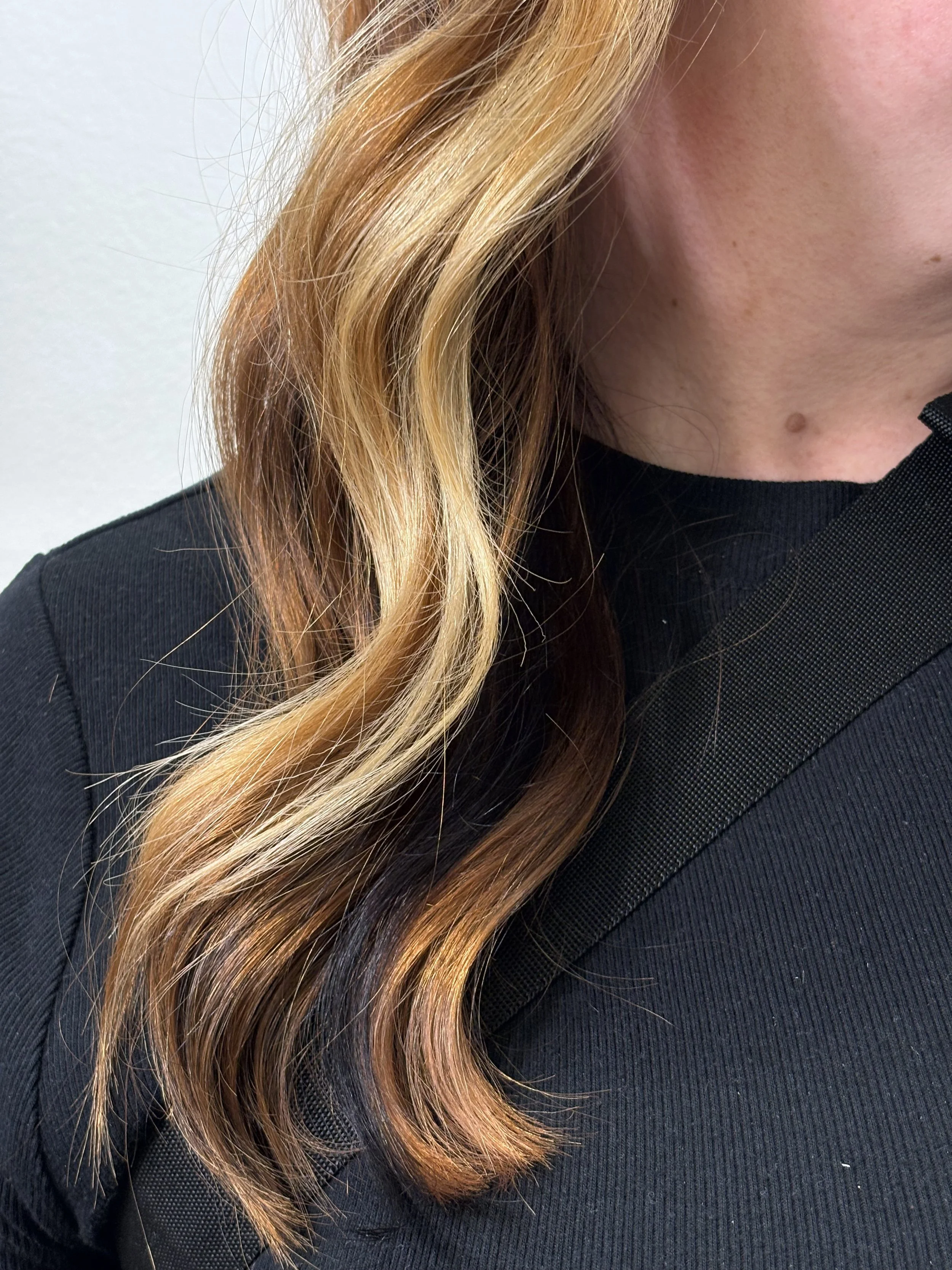 Close-up of a woman's blonde and copper wavy hair, part of her face, and a black textured shirt.