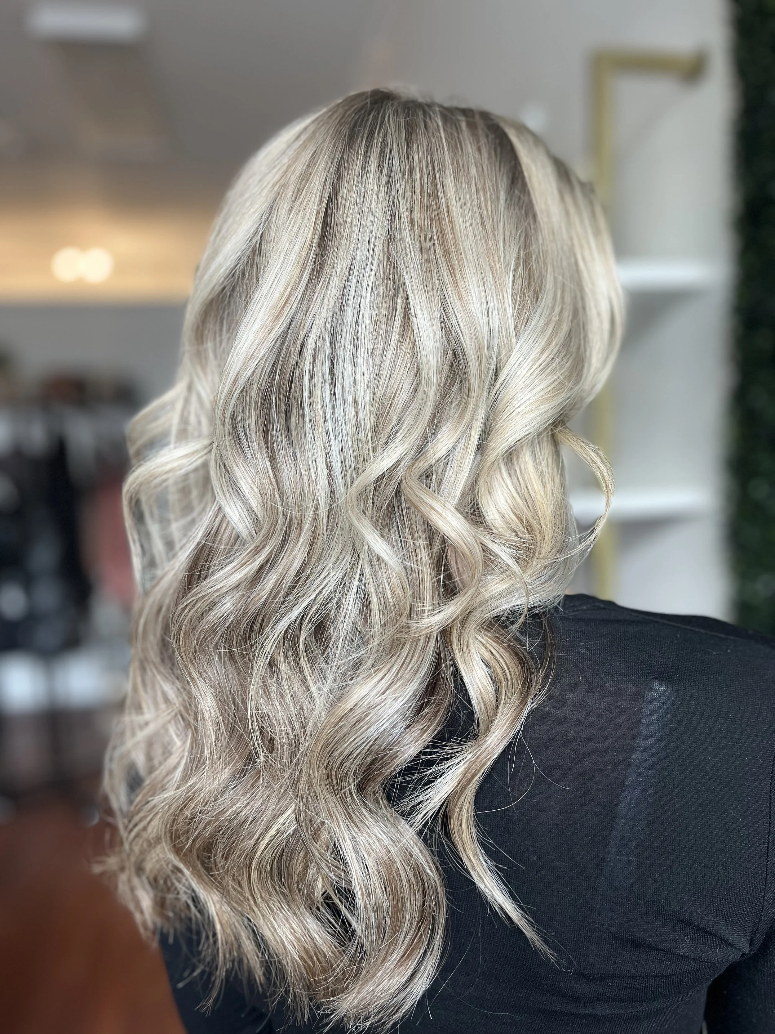 Back view of a woman with long, wavy, blonde hair with highlights.