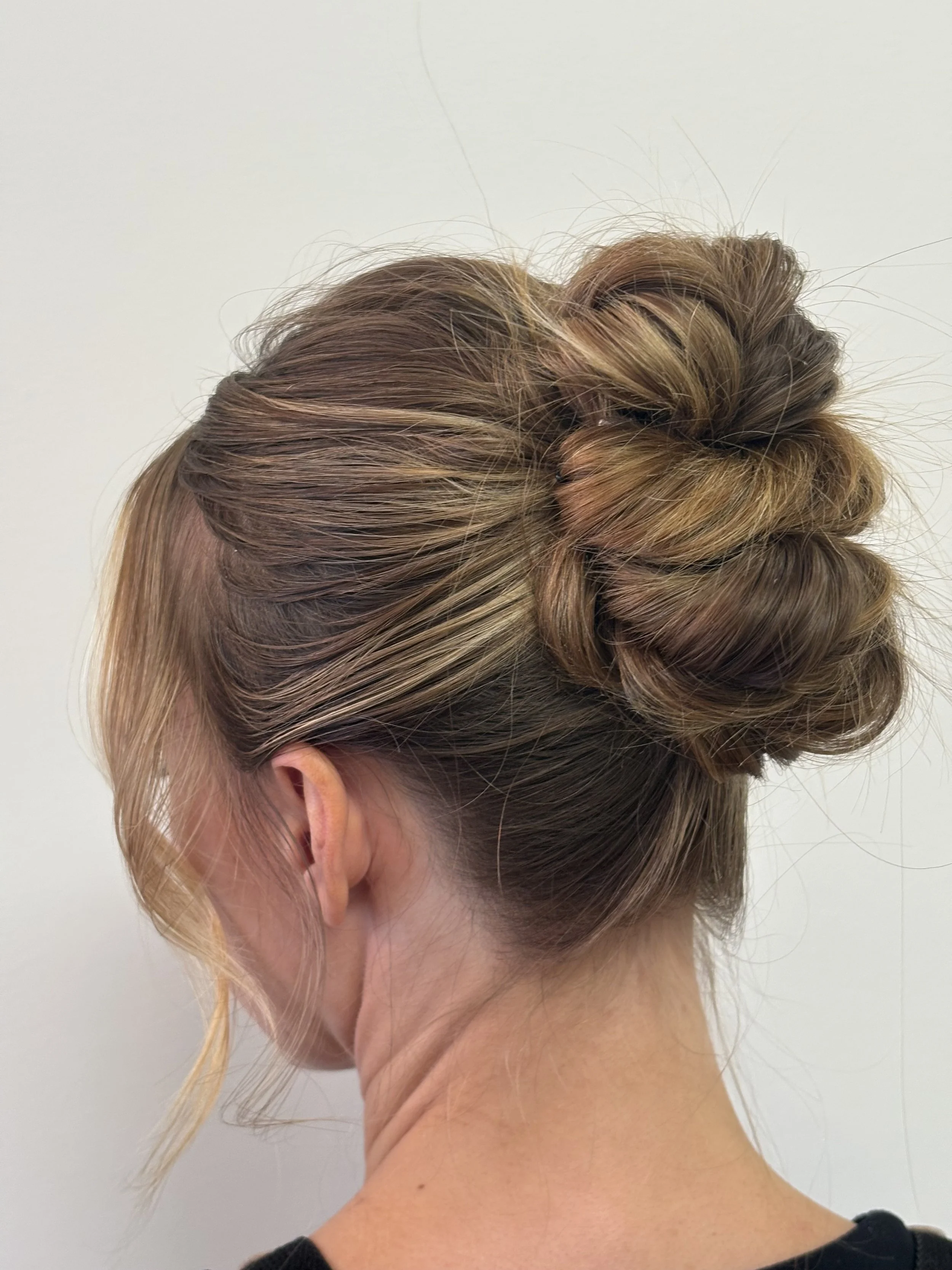 A woman has an updo hairstyle with a twisted bun, styled with hair color shades of blonde and light brown, against a plain white background.