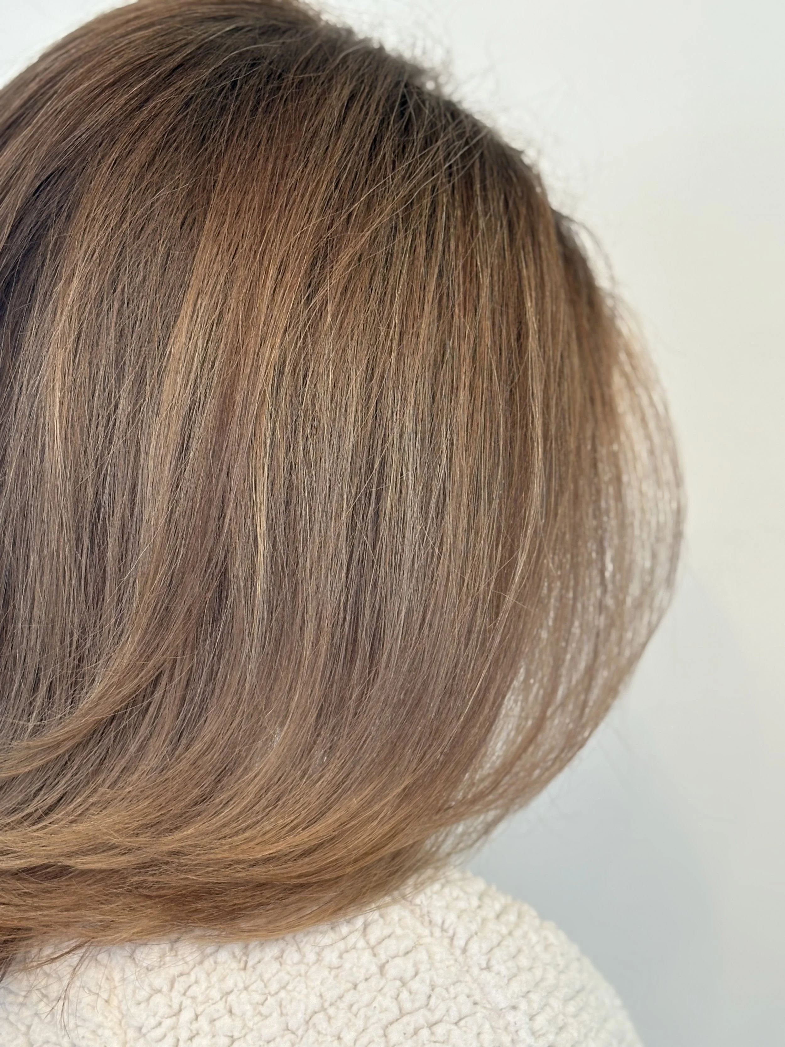 Close-up of a person's head with brown hair and a layered haircut, wearing a cream-colored textured sweater.