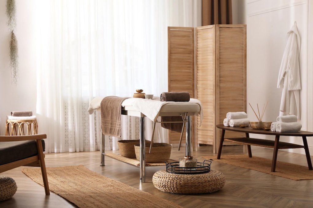Spa or massage room with a massage table, rolled towels, a wooden privacy screen, and calming decor.
