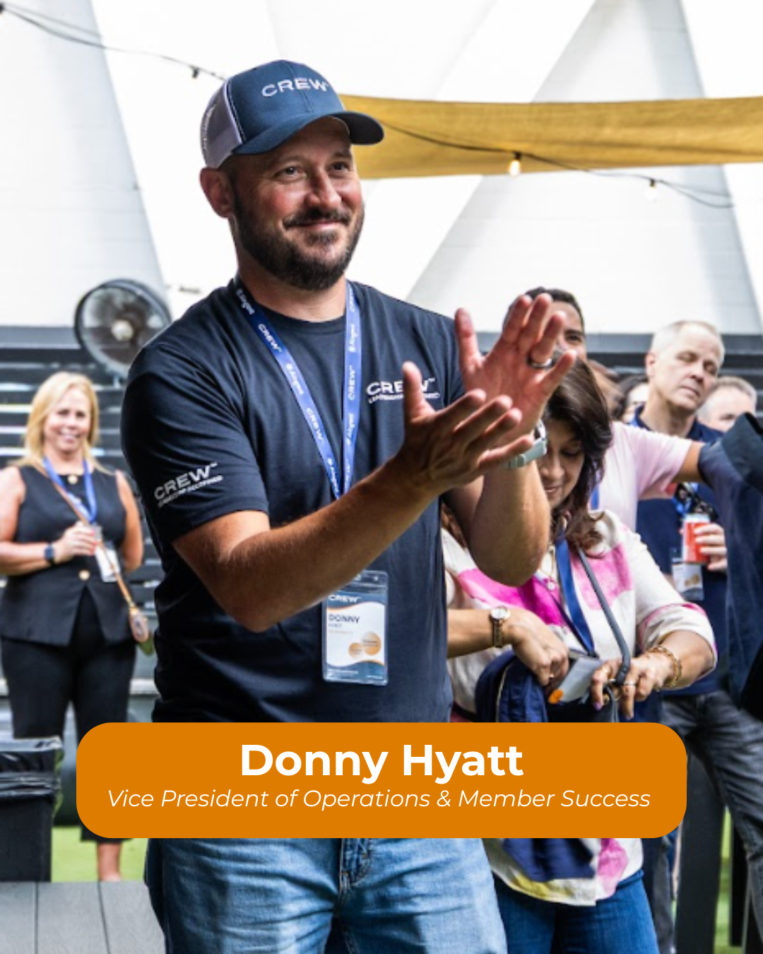 A man wearing a baseball cap and a navy T-shirt with the word 'CREW' on it, smiling and clapping at an indoor event with multiple people around him. The image has a name tag that reads 'Donny Hyatt' and the title 'Vice President of Operations & Member Success.'