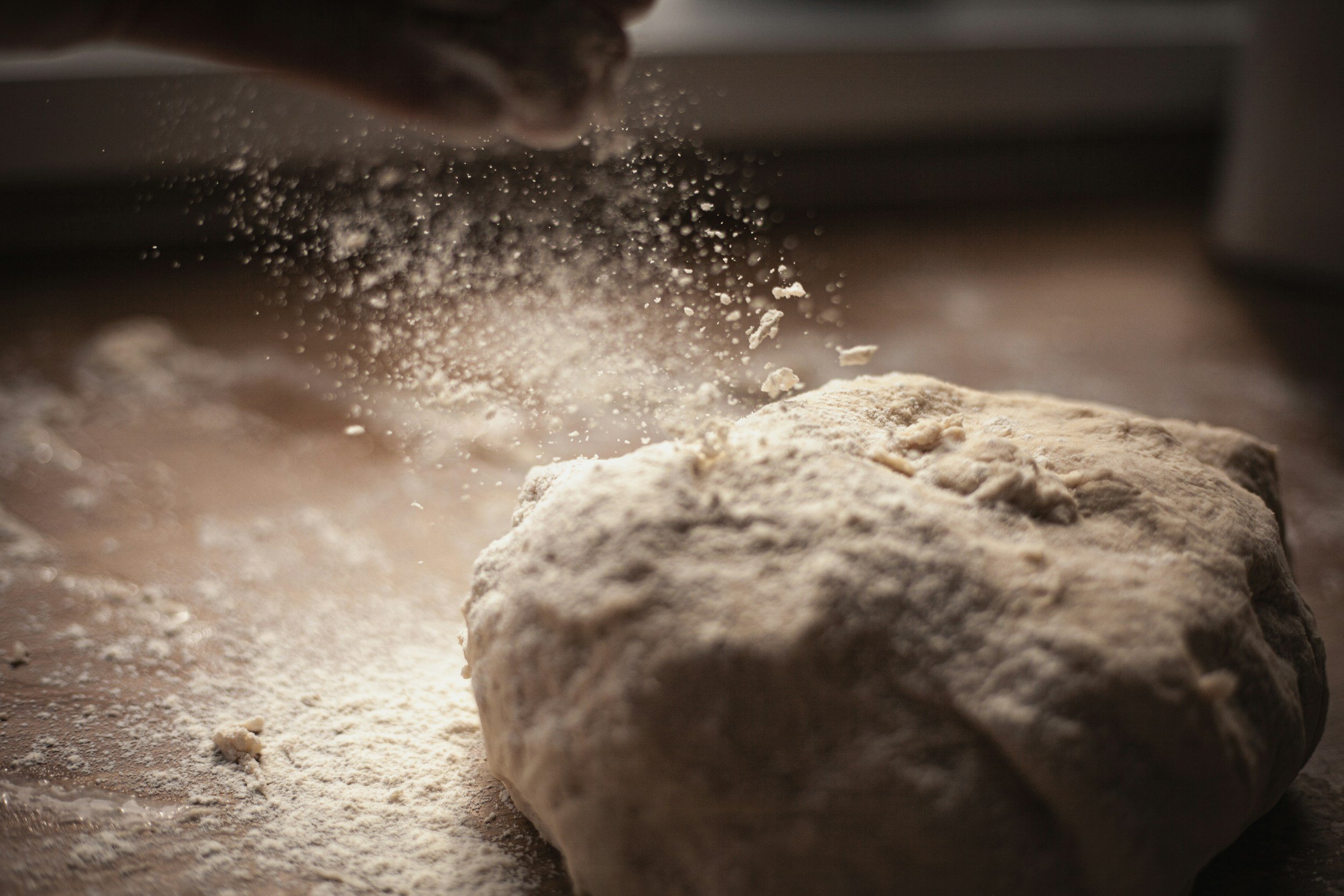 Close-up of dough or flour on a work surface with a hand sprinkling flour over it.