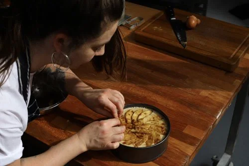 Woman preparing a dessert in a round baking dish on a wooden countertop.