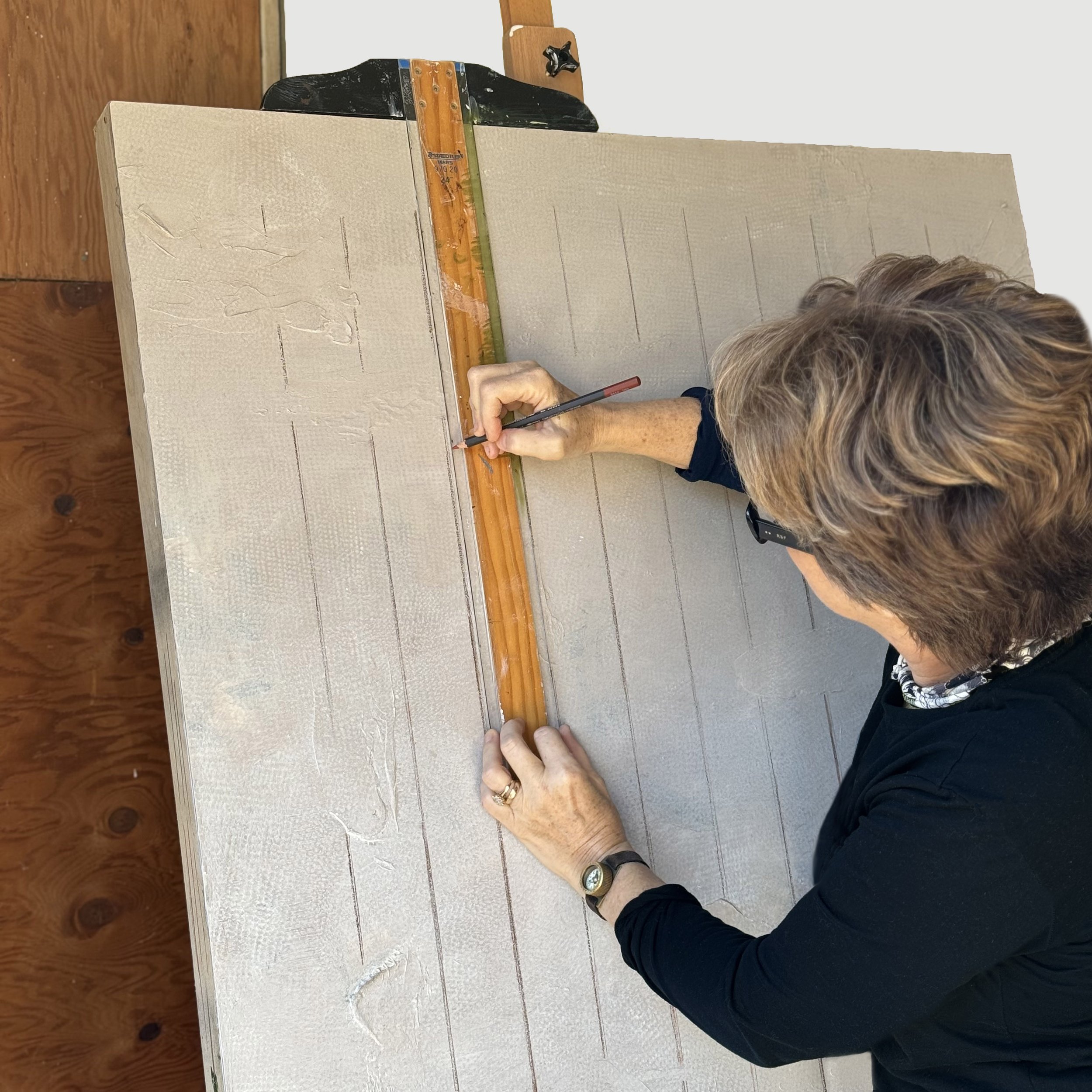 Person drawing on a large wood panel, using a wooden level as a straight edge.