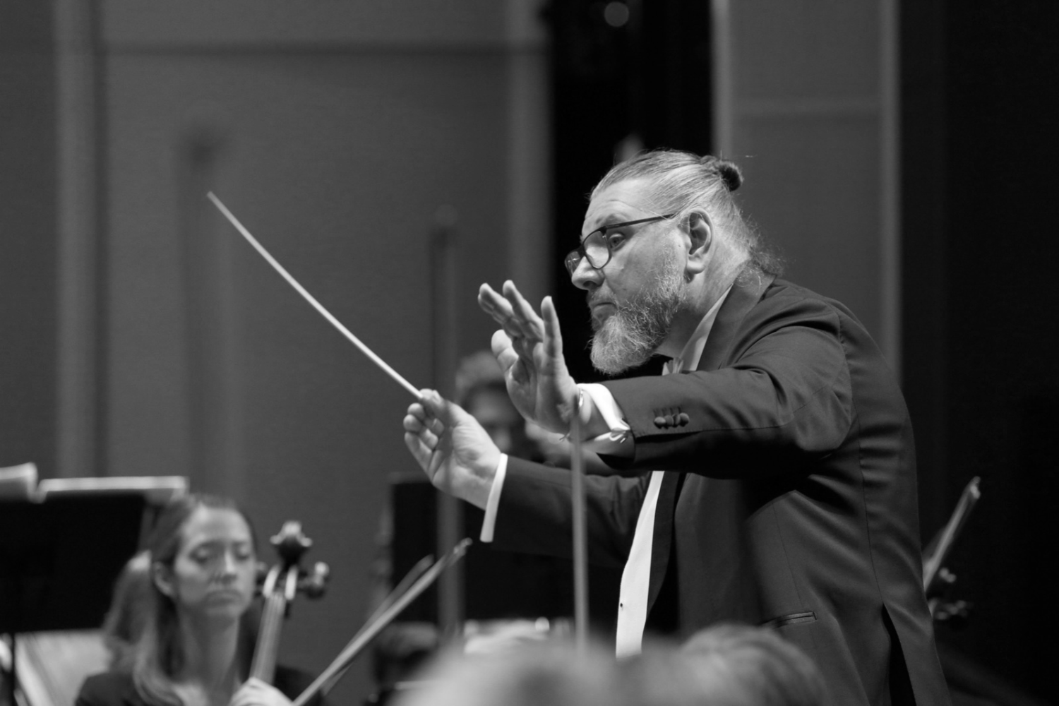 Conductor Daniel Henriks leading an orchestra in performance, with baton in hand and string musicians behind him.