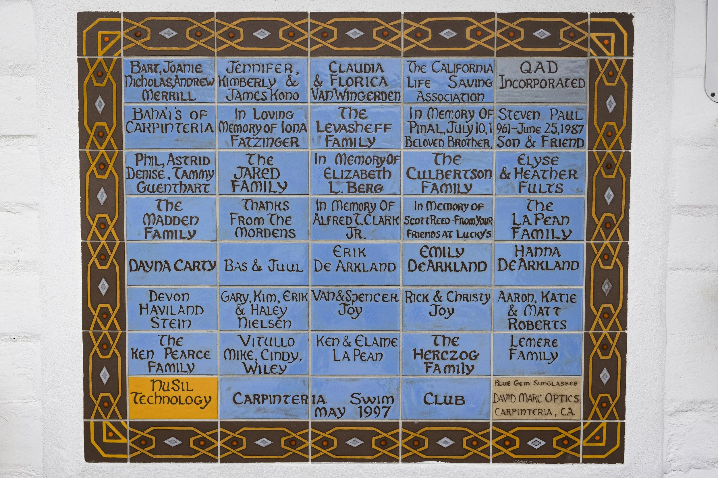 A commemorative tile wall featuring multiple names of individuals, families, and organizations, with a decorative border, including a yellow section labeled 'Music Technology' and a note at the bottom mentioning 'Carpinteria, May 1997' and 'Swim Club'.