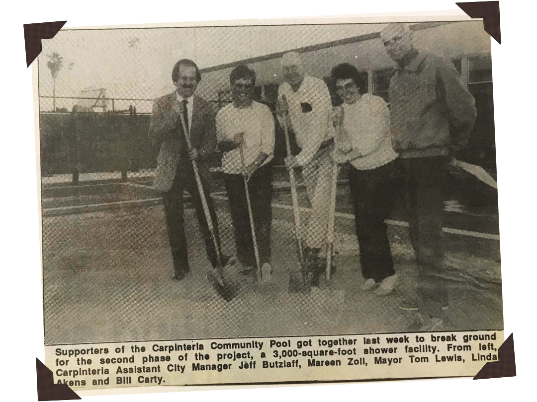 Black and white photo of six people standing outdoors in front of a building, holding shovels and a wheelbarrow, at a groundbreaking ceremony for a new community pool shower facility. The caption mentions the event, location, and names of the participants.