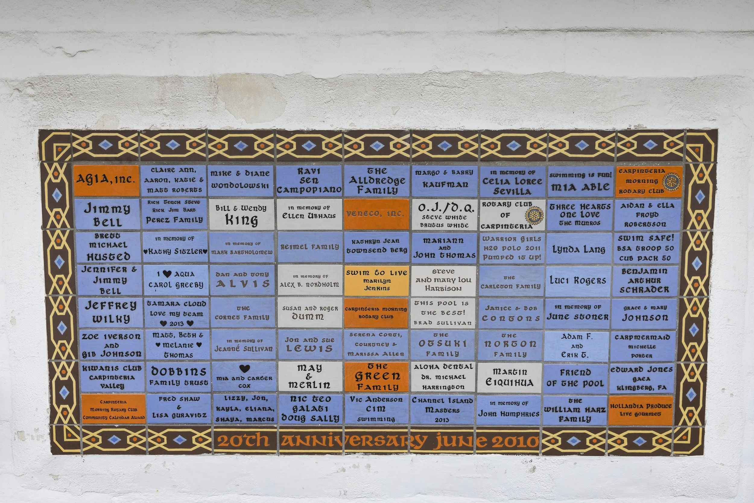 A decorative plaque commemorates the 20th anniversary of a rotary club, with names of members and in memory of individuals, arranged in a grid with a black, brown, and blue patterned border.