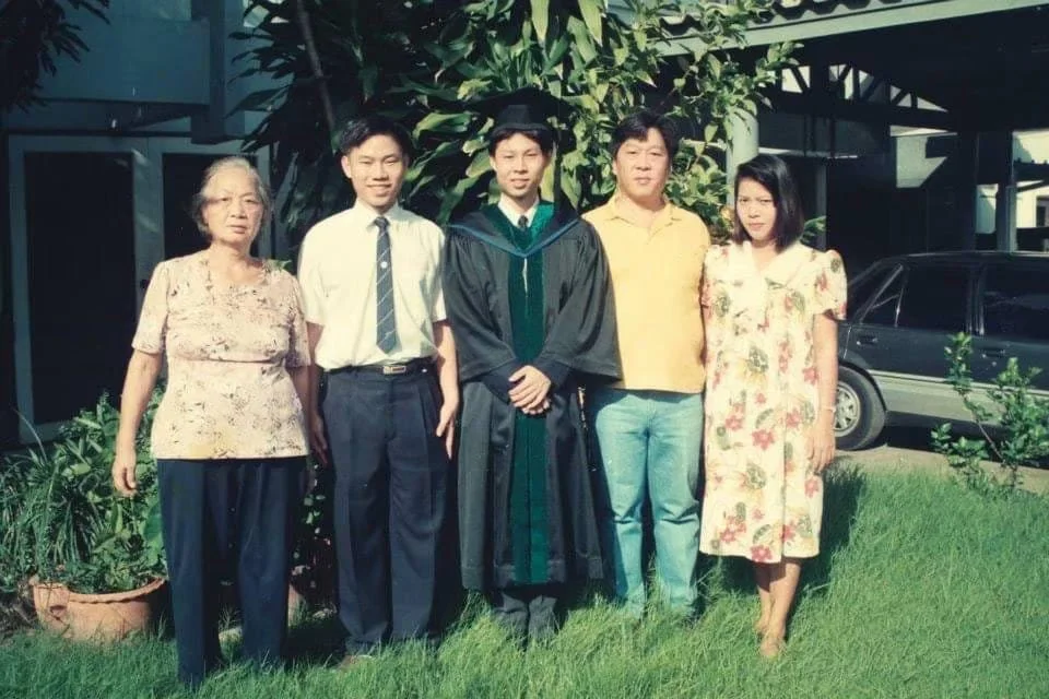 Family posing outdoors with a graduate wearing a black academic gown and green stole