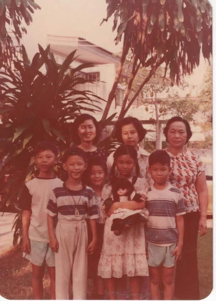Vintage family photo of women and children posing outdoors in front of tropical plants