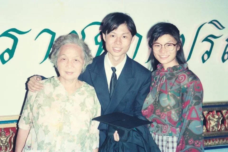 Three people pose together, with a graduate in a suit holding a graduation cap between two women.