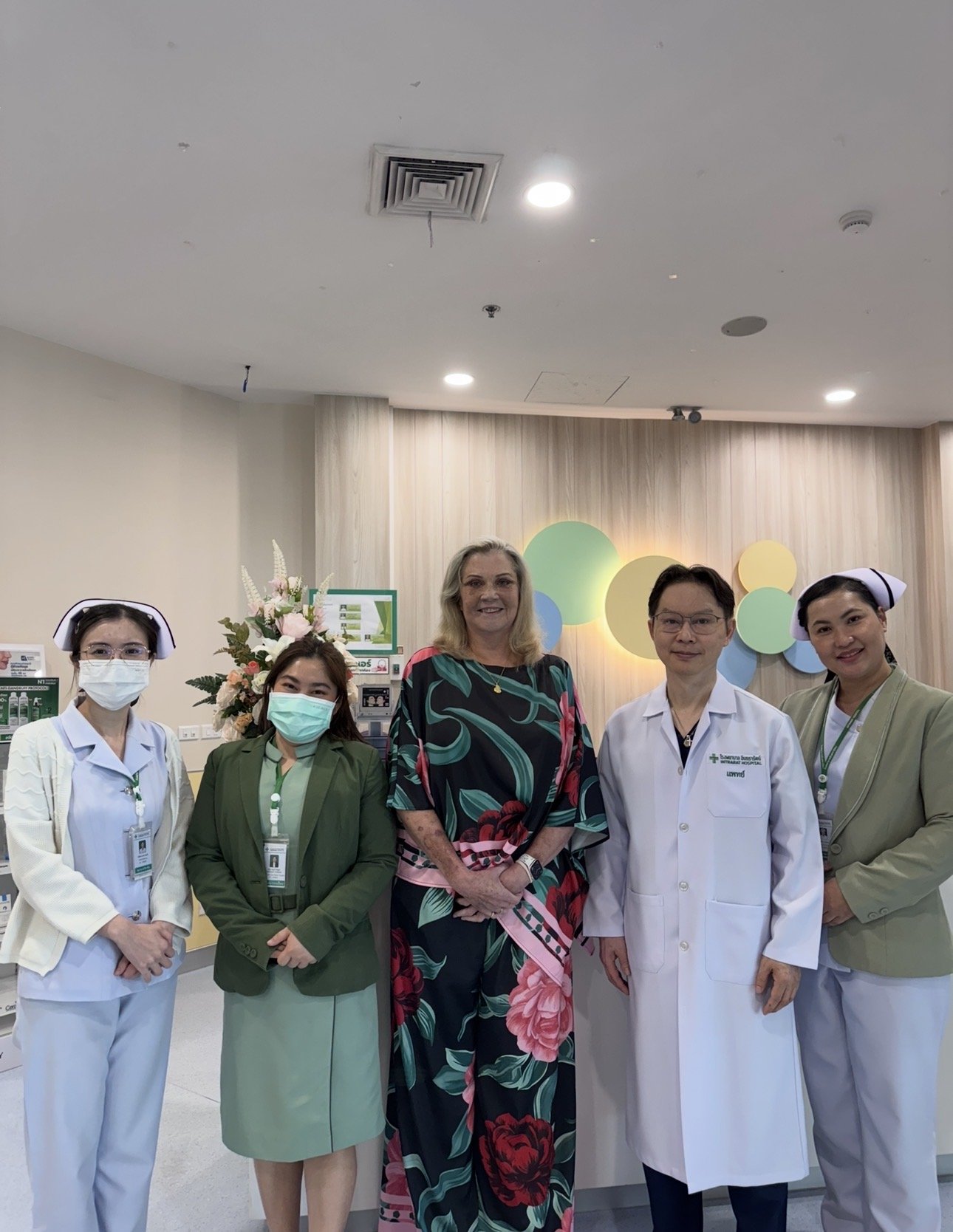 Hospital staff and a woman in a floral dress posing together in a hospital lobby