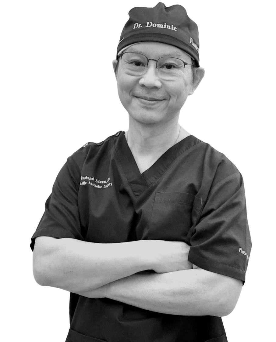 A smiling person wearing medical scrubs and a hat with the text 'Dr. Dominic' on it, standing with arms crossed.