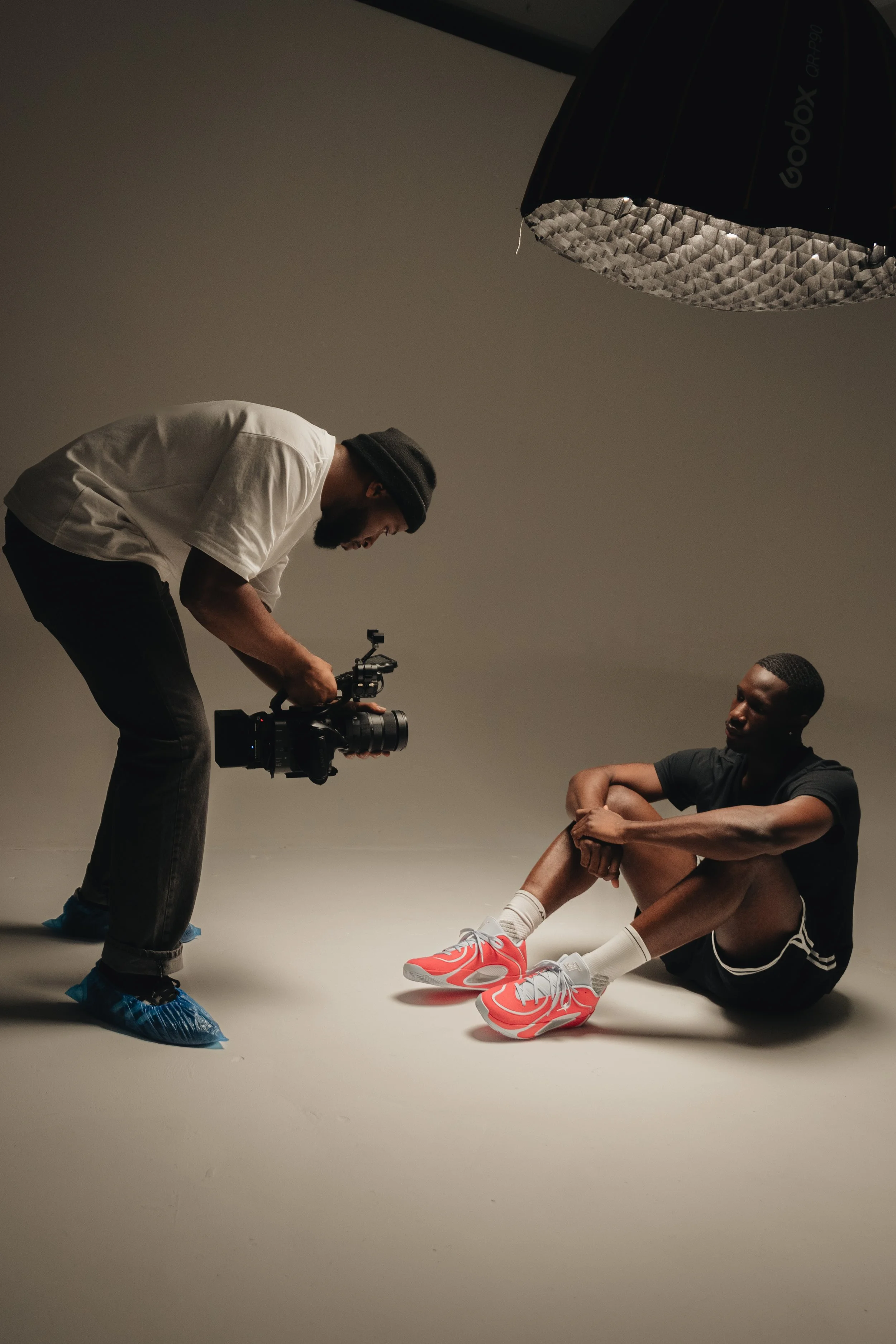People working on a film set with camera equipment, lights, and rigging inside a large studio with a white backdrop and overhead grid.