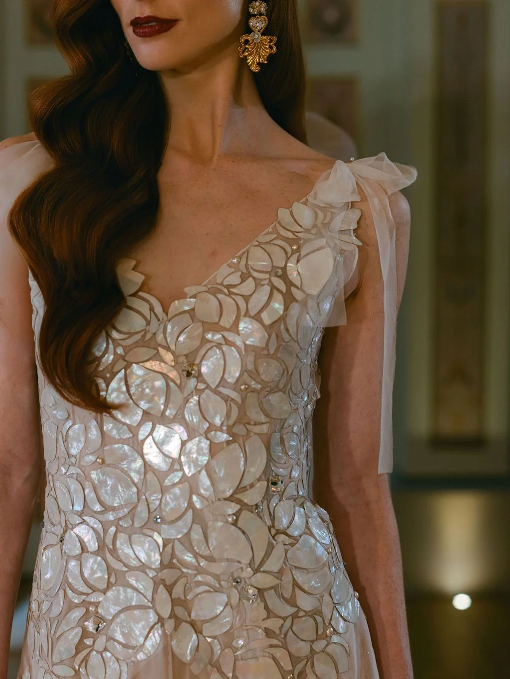 Close-up of a woman wearing an elegant dress with a floral, shell-like pattern, and large, ornate gold earrings.
