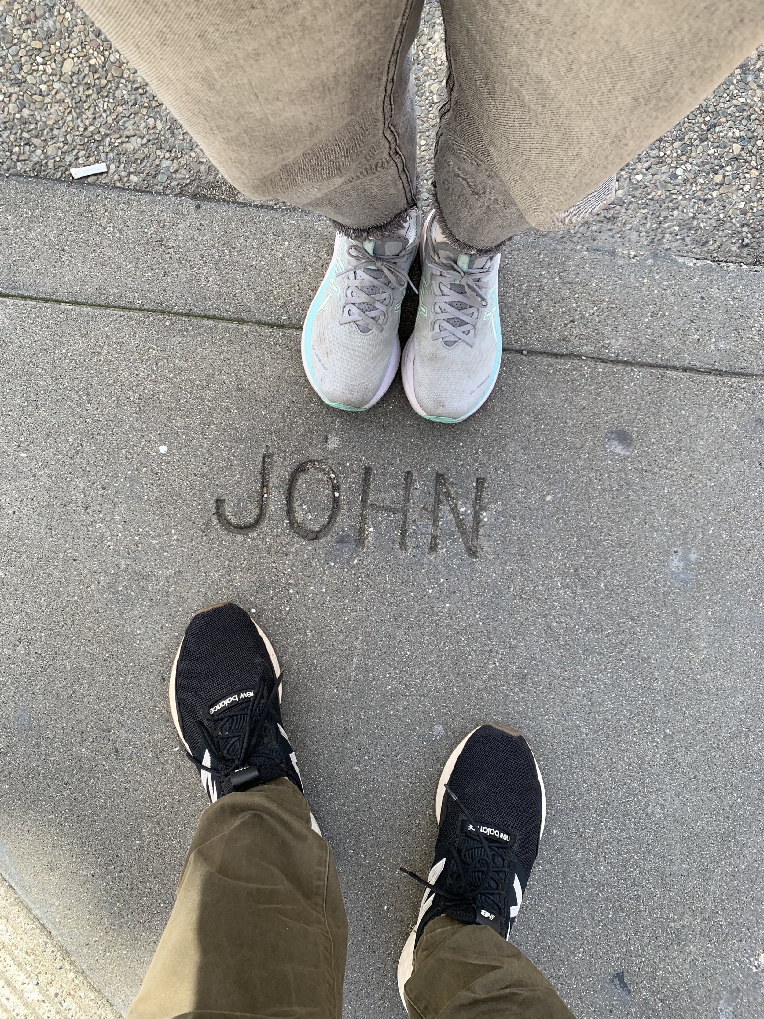Decorative photograph of two sets of sneakered feet standing over word JOHN written in concrete