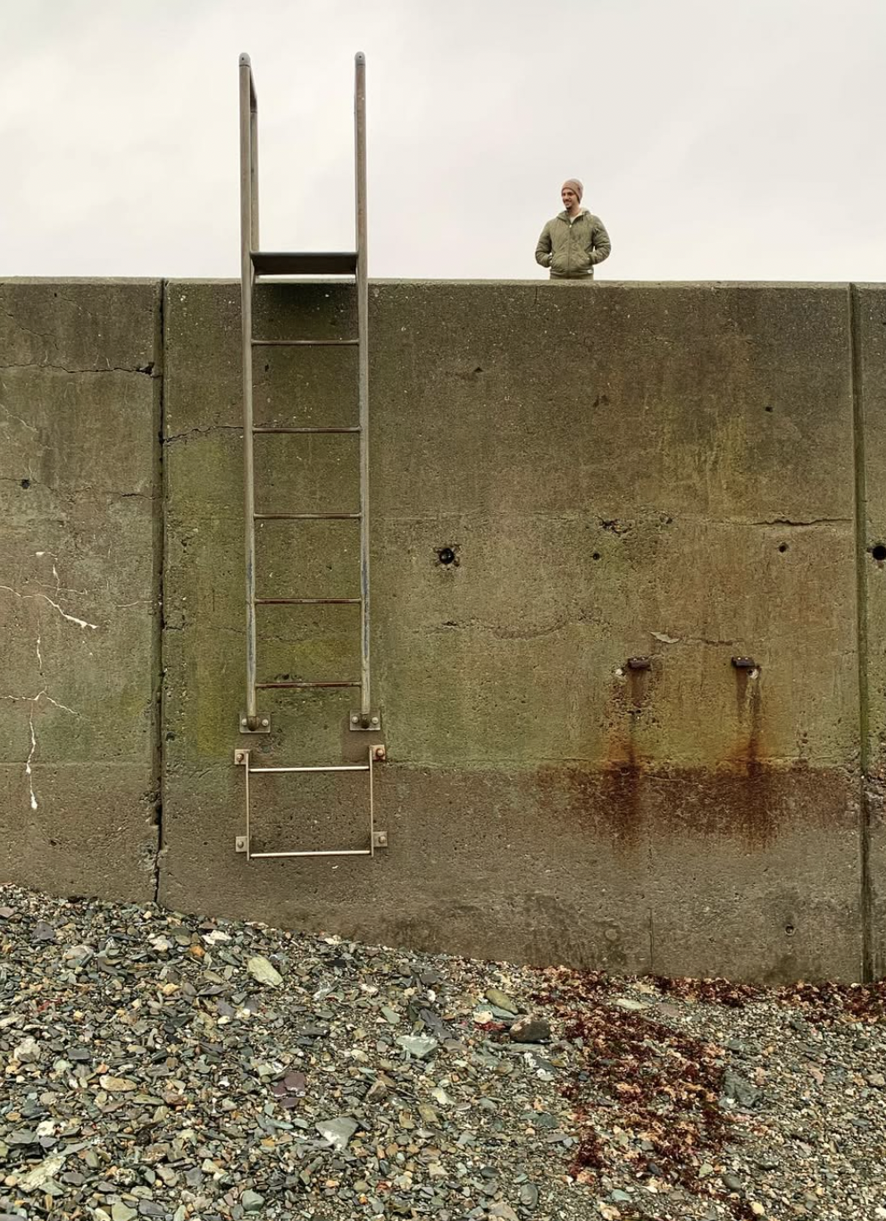 Decorative photograph taken by the author of the author's brother standing over a wall with a metal ladder leading down to rocks