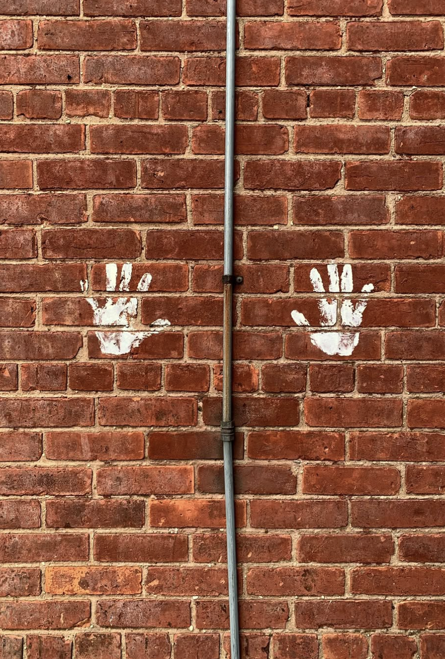 Decorative photograph of a brick wall marked with two handprints painted in white