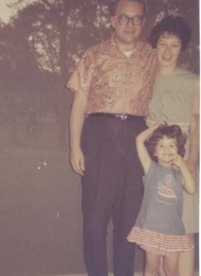 A man, a woman, and a child stand in front of trees seen through screening.