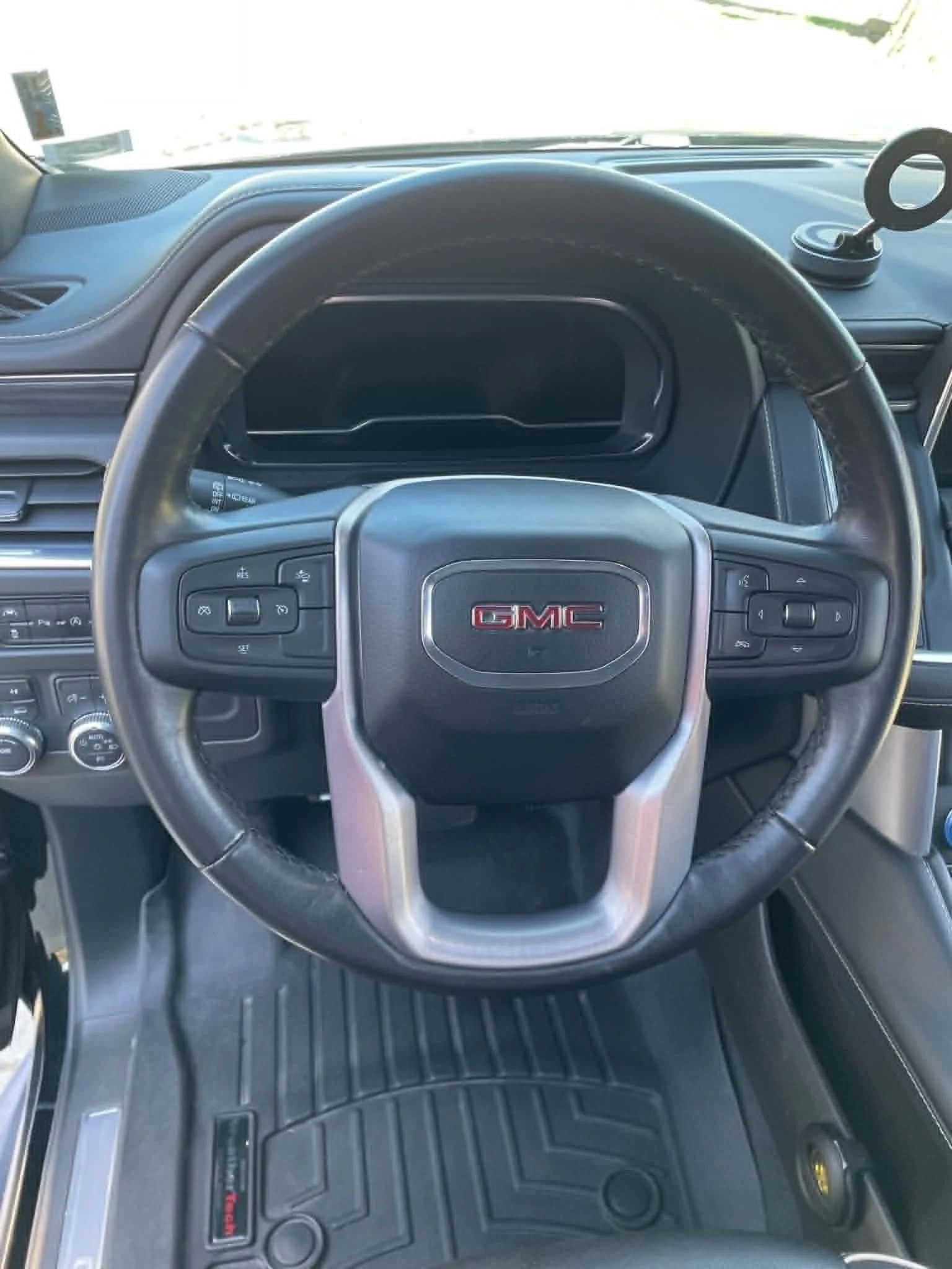 Interior of a GMC vehicle showing steering wheel, dashboard, and dashboard accessories, with a black rubber floor mat.