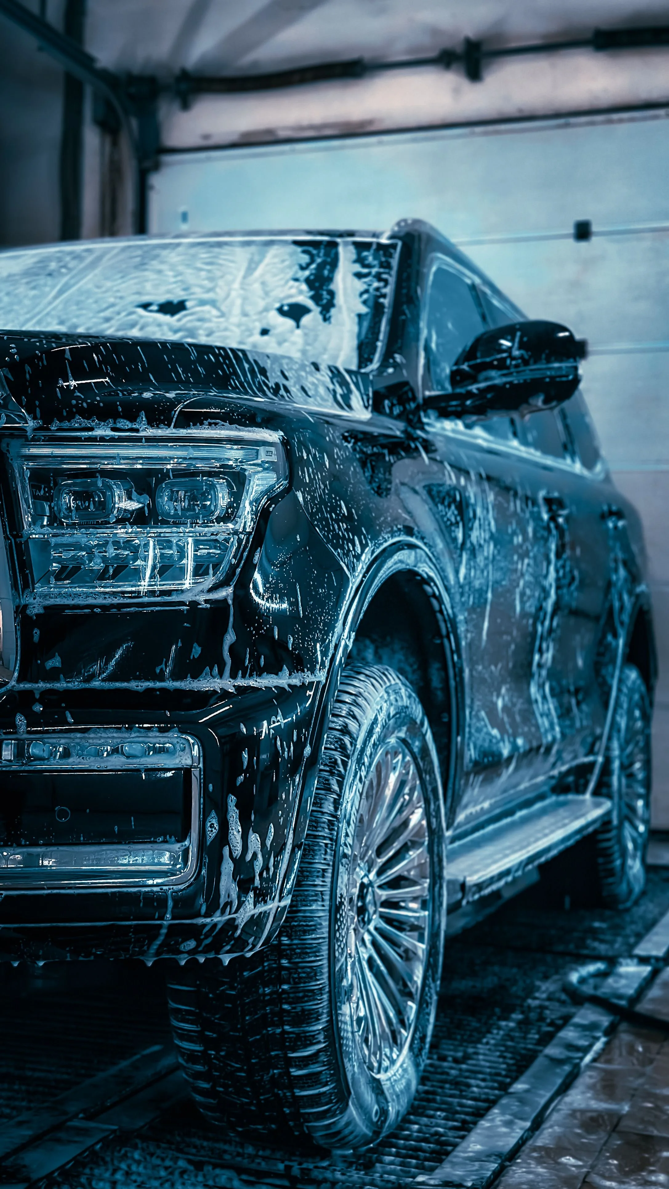 Black luxury SUV getting washed with soap and water in a car wash station.