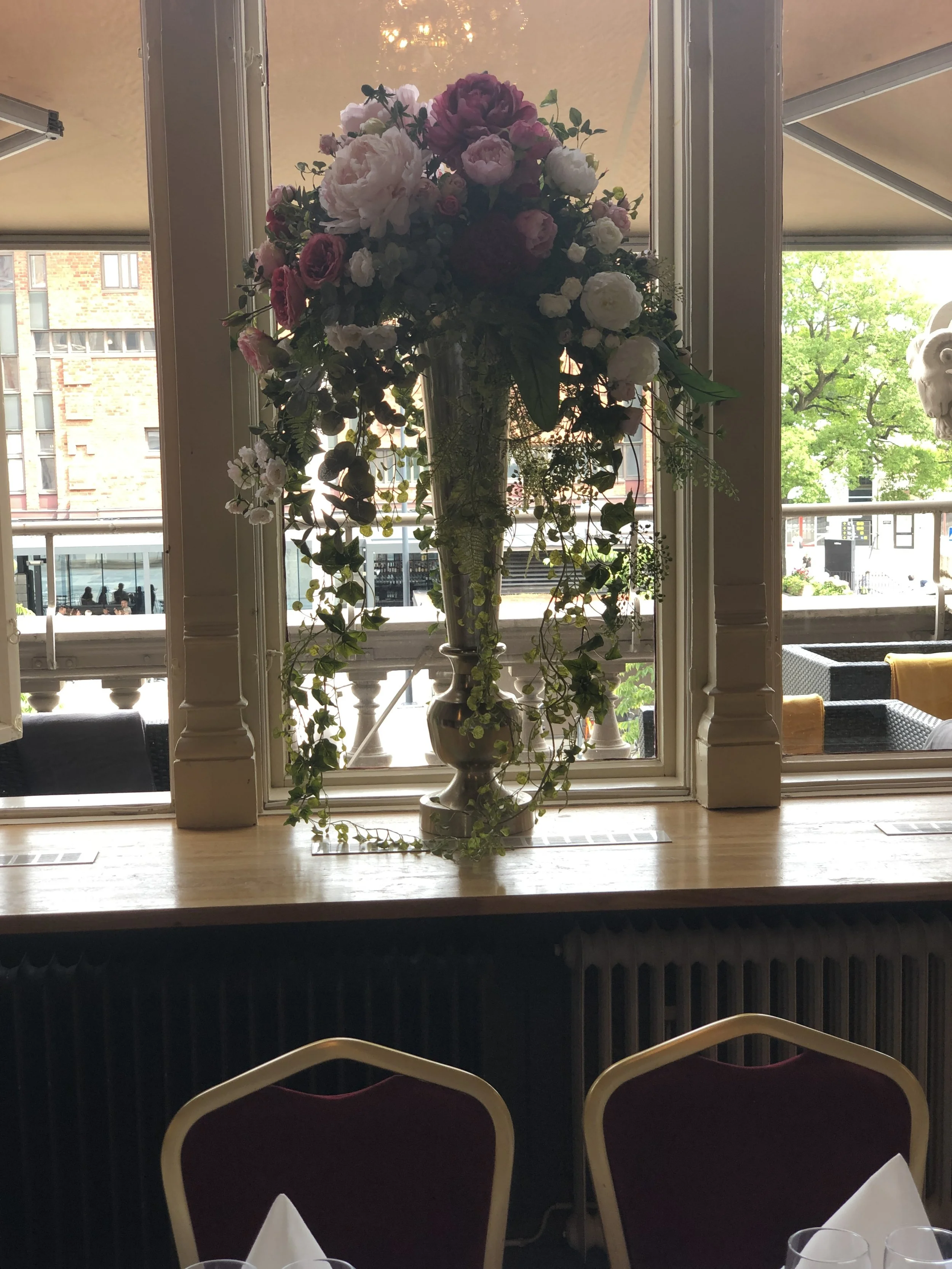 Stort blomsterarrangemang med vita, rosa och lila blommor från Studio Mjölk, placerat framför fönster.
