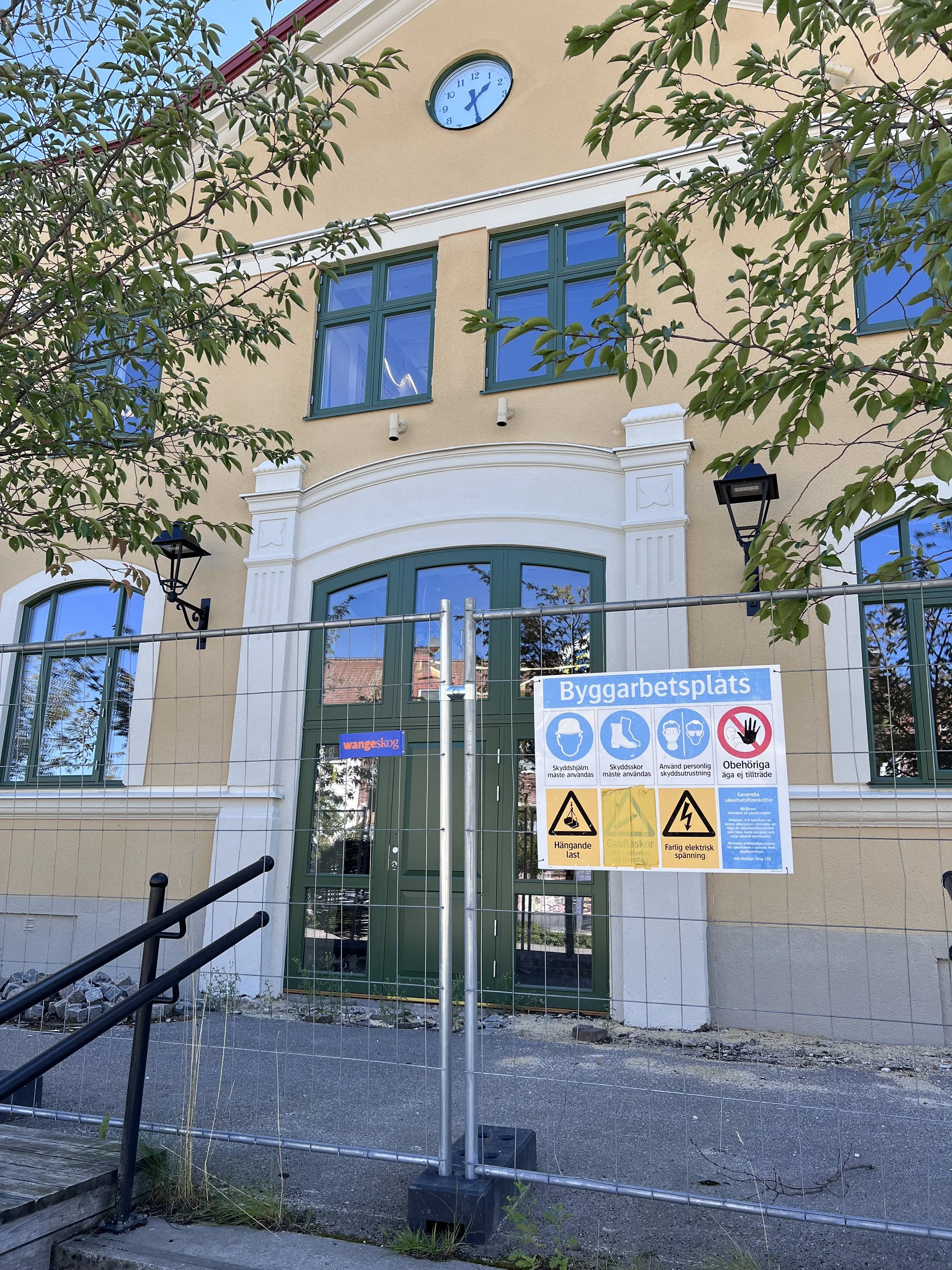 Byggarbetsplats med informationsskylt, staket och byggutrustning.
