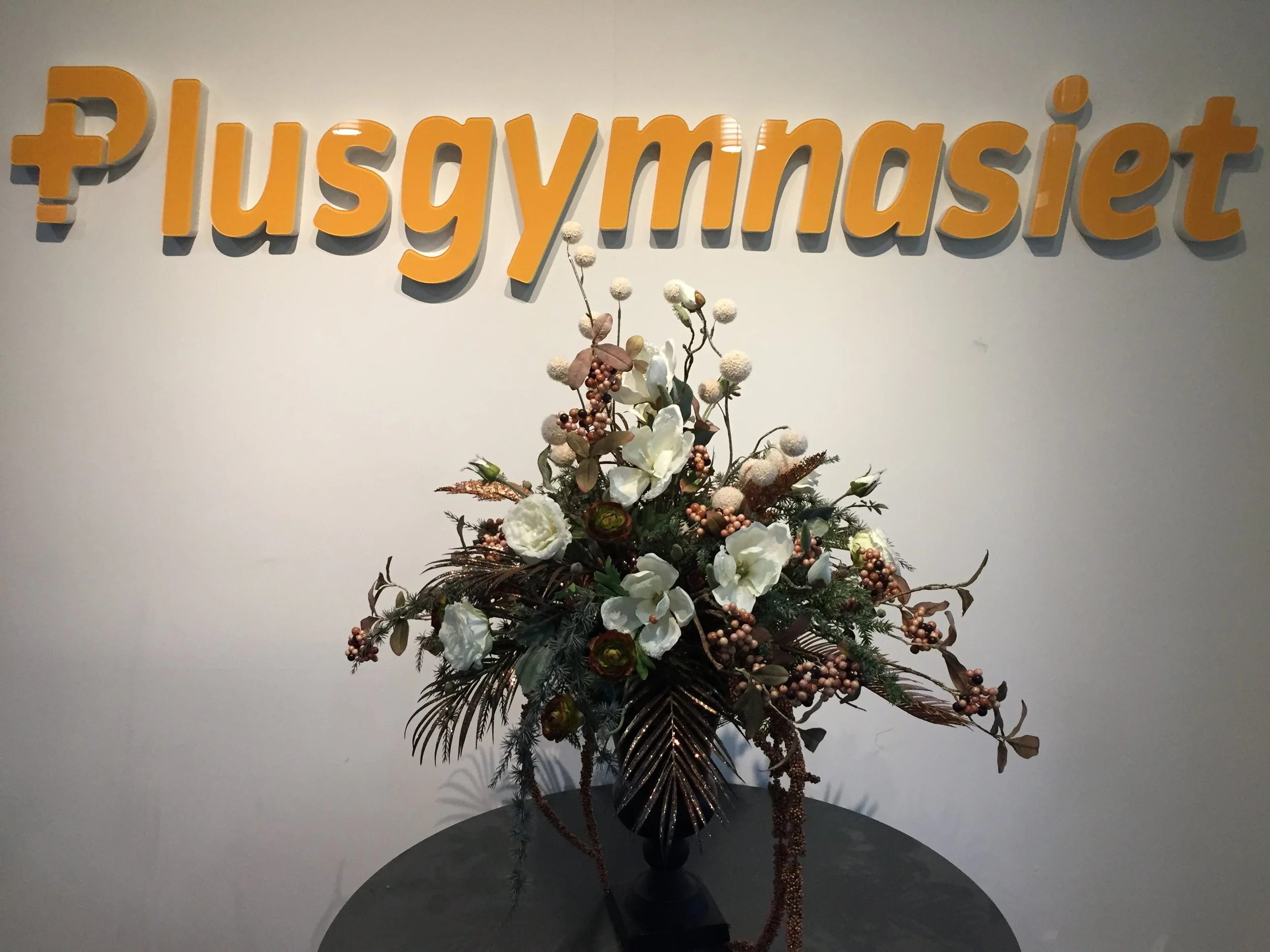 Blomsterarrangemang med vita blommor och gröna inslag, skapat av Studio Mjölk för Plusgymnasiet.
