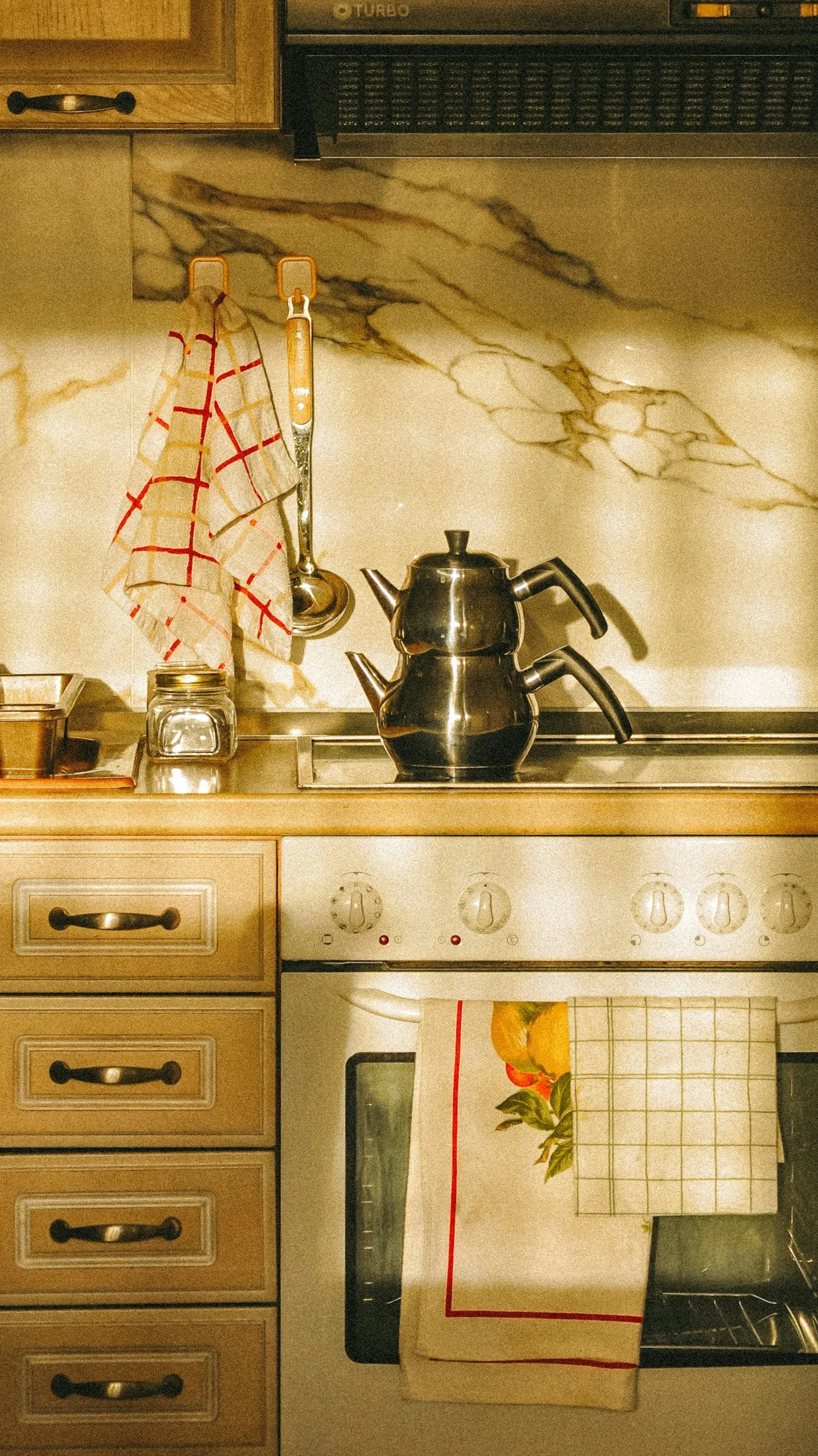 Sunrise in your kitchen; A kitchen countertop with a landline oven, a vintage tea-towel hanging on a hook, and a silver percolator making coffee for the day.