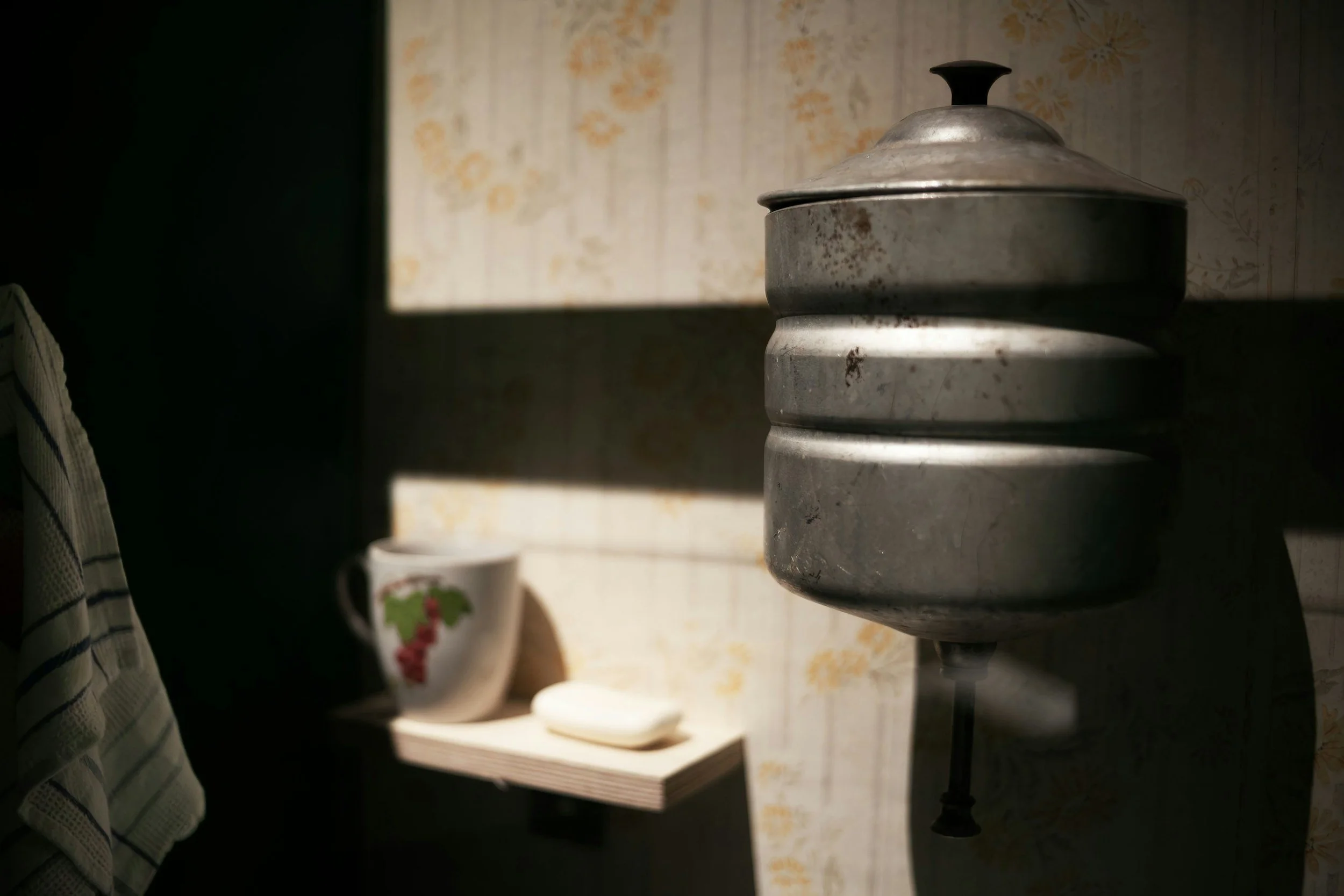 Old metal weight scale on a dark table in front of floral wallpaper.
