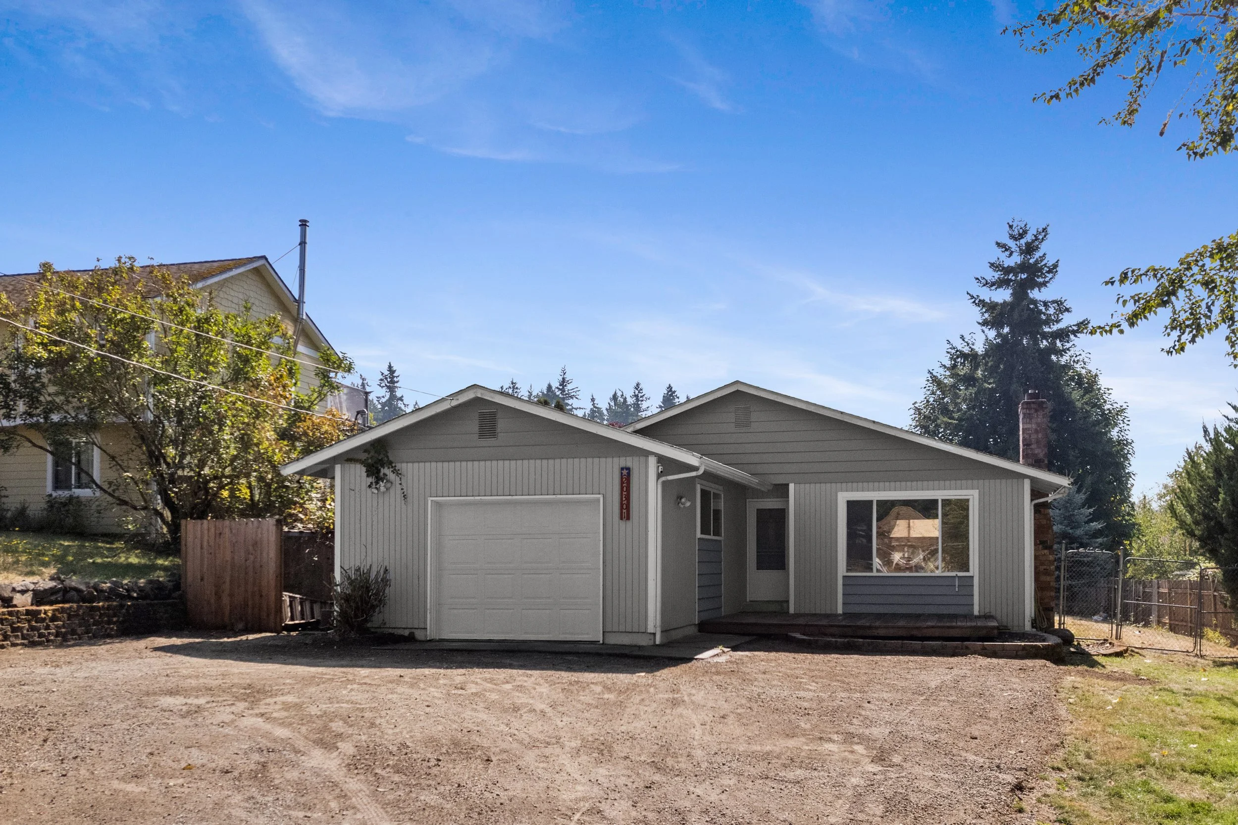 Backyard scene with a small white garage, a house in the background, trees, and a clear blue sky.