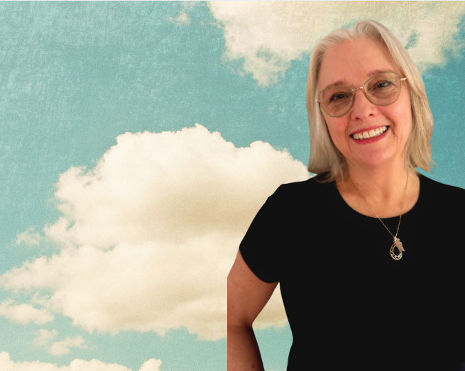 Valerie- Root Real Estate Broker smiling against a sky and clouds background.