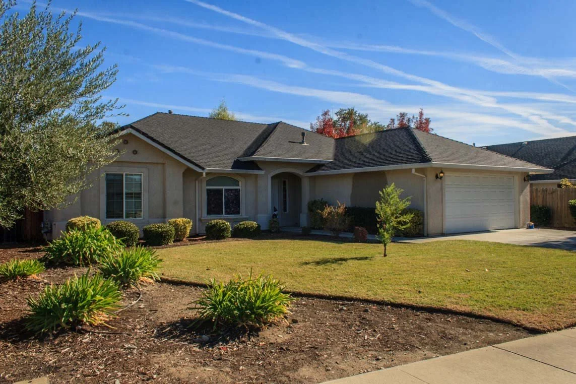 A single-story house with a manicured lawn and garden, blue sky with wispy clouds.