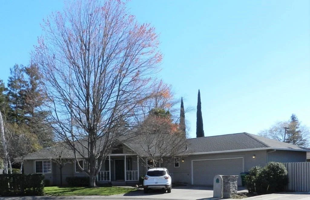 Single-story house with a front yard, leafless tree, parked white SUV, and a driveway in a suburban neighborhood.