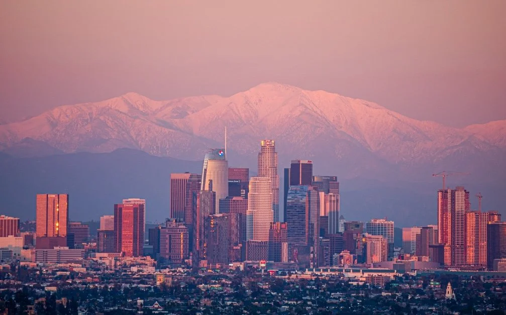Los Angeles skyline with snow-capped mountains in the background at sunset.