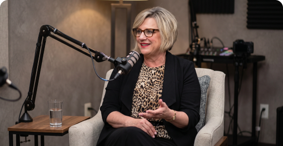 Woman wearing glasses speaking into a microphone during a podcast interview