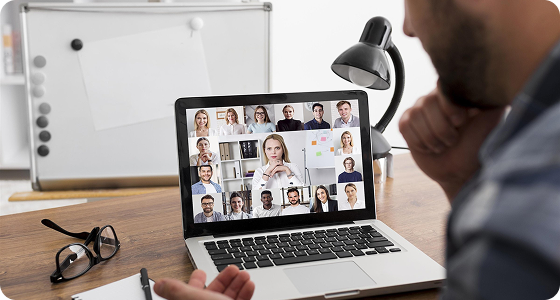 Business professional viewing a laptop video conference with multiple remote colleagues at a desk