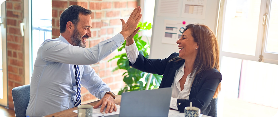 Smiling business professionals high-fiving across a desk with a laptop in a bright office