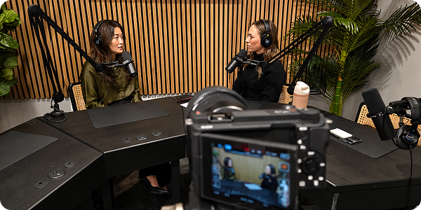 Two women recording a podcast in a studio with microphones and a camera