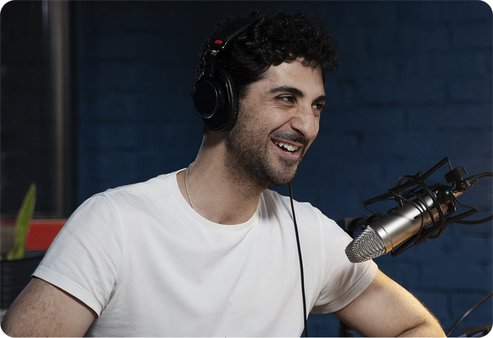 Smiling man wearing headphones speaking into a studio microphone