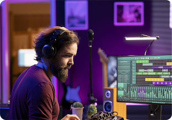 Bearded audio engineer wearing headphones while mixing music on a digital audio workstation in a purple-lit recording studio