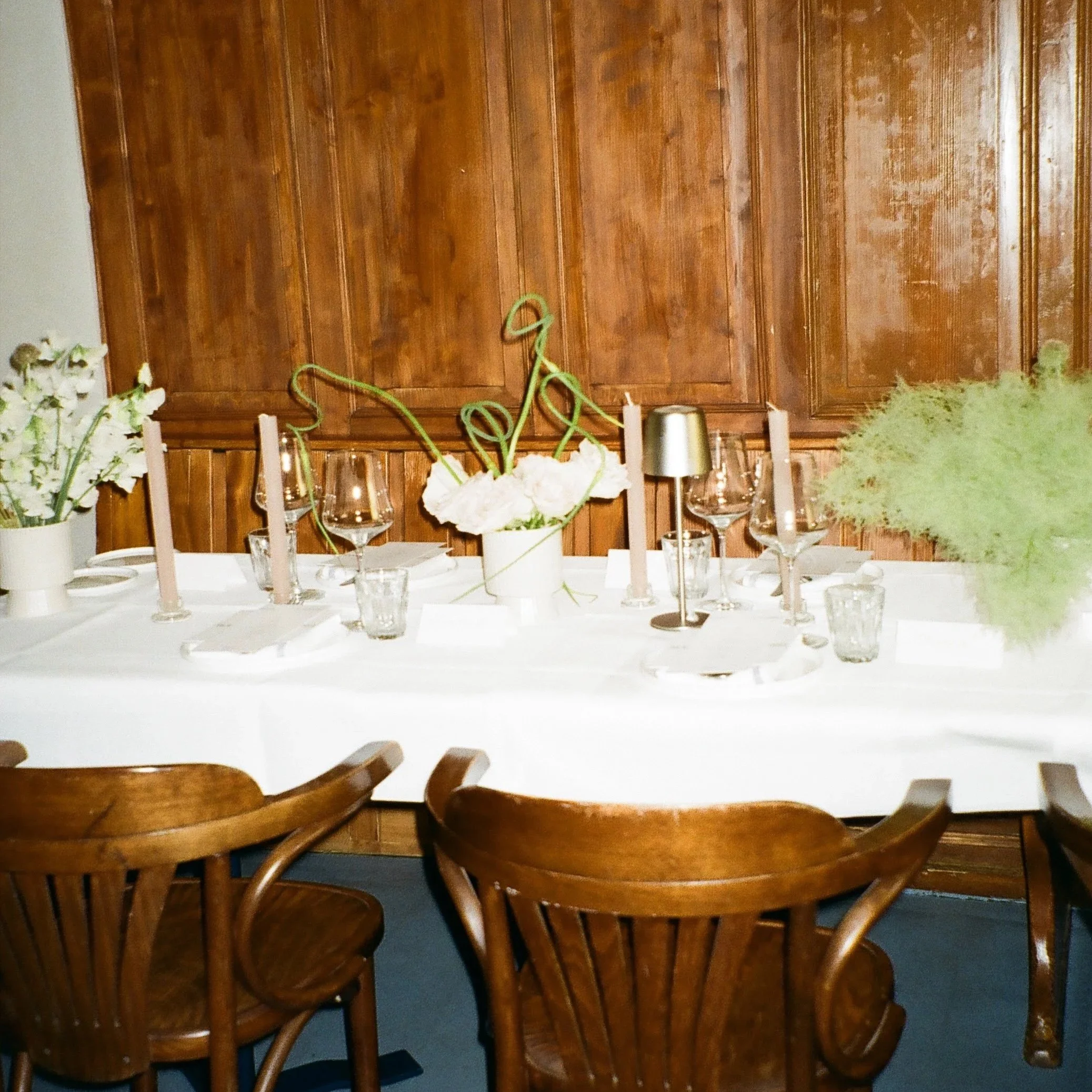 A dining table with wooden chairs, floral centerpiece, and tableware in a room with a wooden wall.