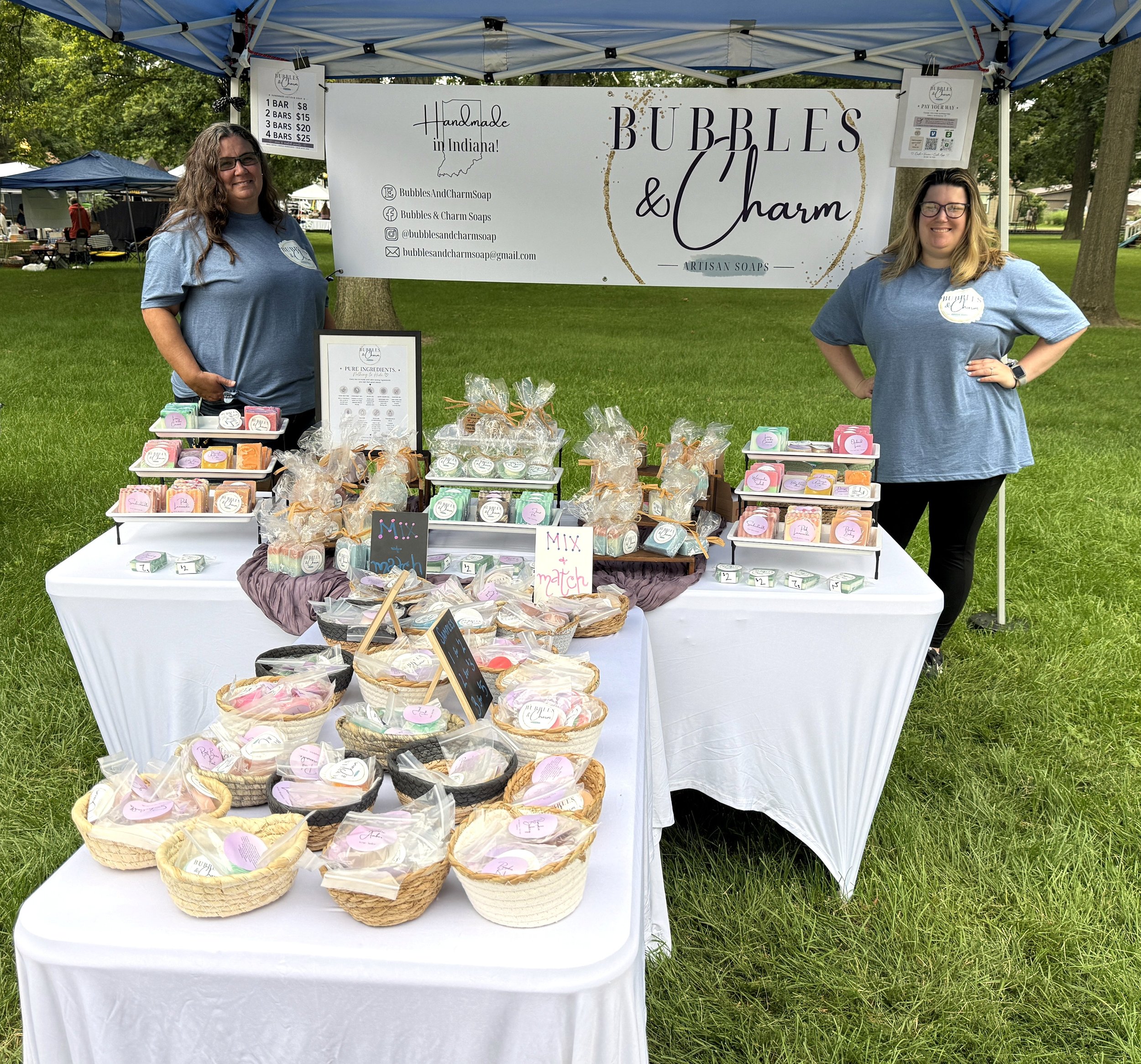 Bubbles & Charm Soaps booth at an outdoor artisan market featuring handcrafted soaps.