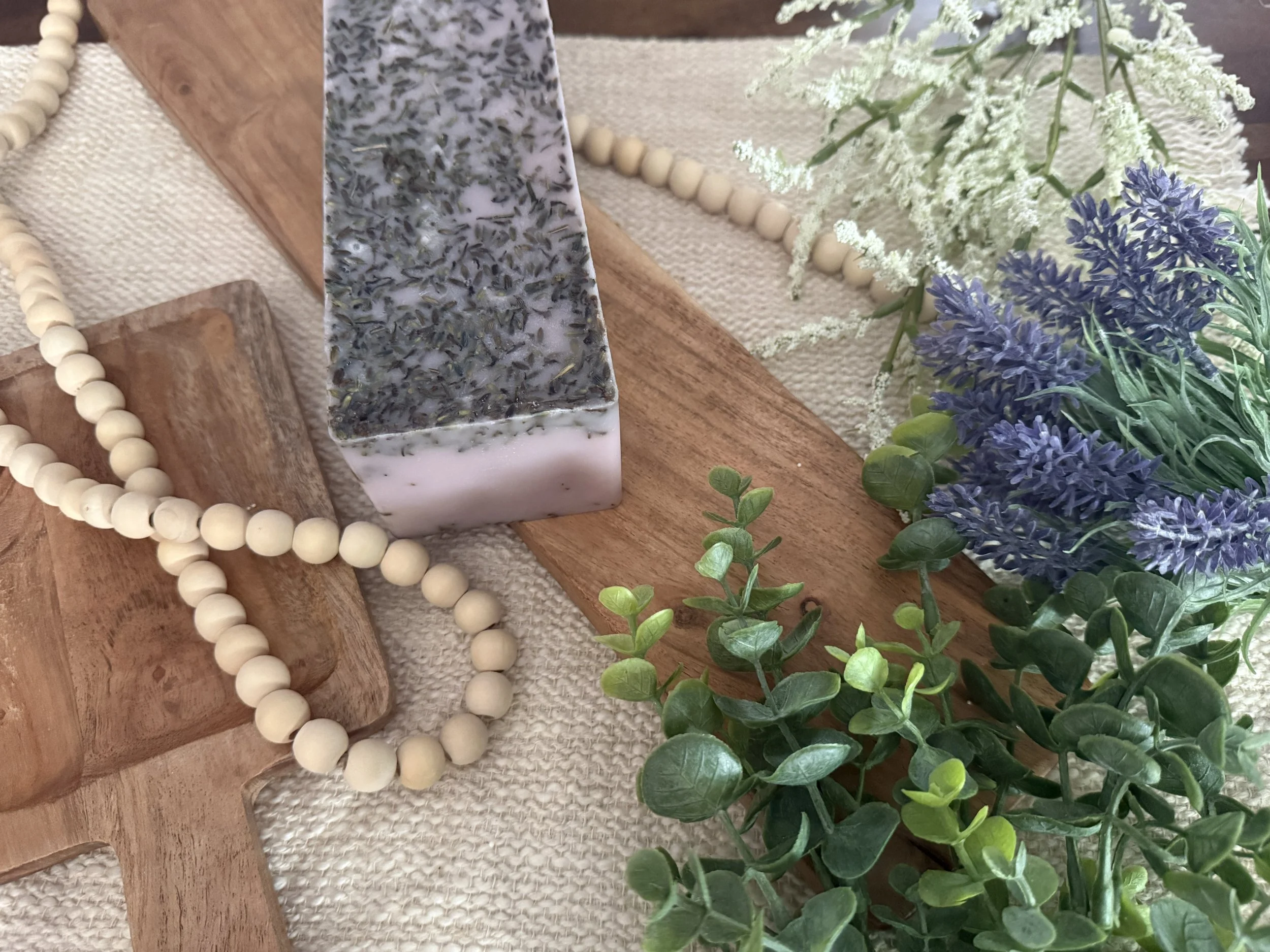 Decorative arrangement of white and purple flowers, wooden and fabric surfaces, and a string of white beads.