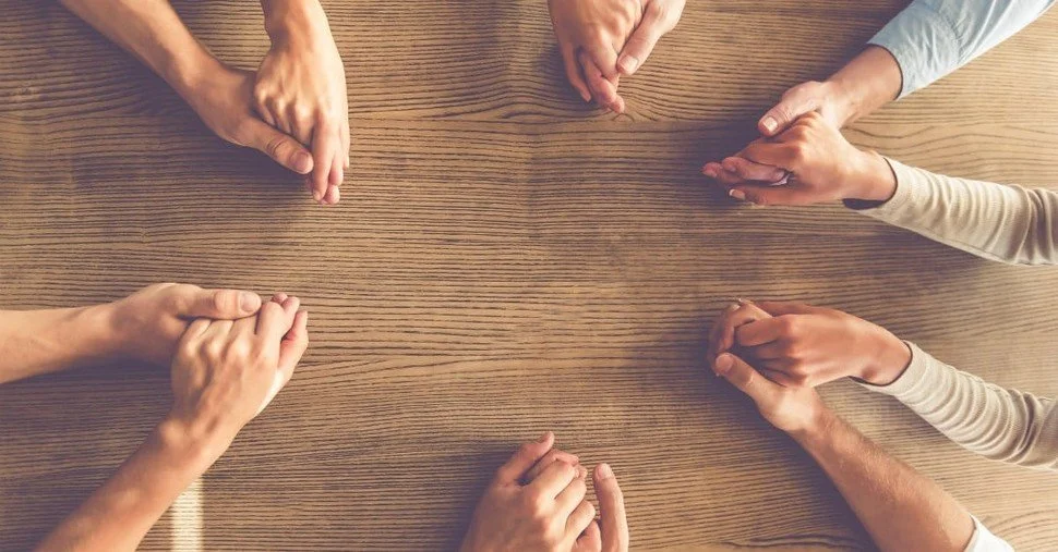 Multiple hands united in a circle on a wooden table, symbolizing unity or teamwork.