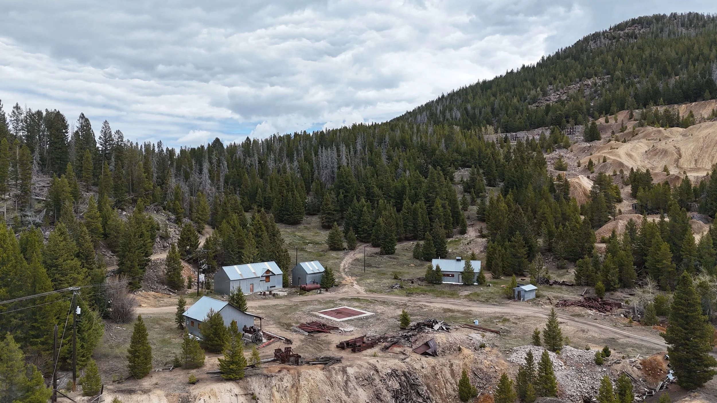 Martin aerial drone Mountains covered with dense green trees with some slope areas and a few small buildings at the base, under a cloudy sky.