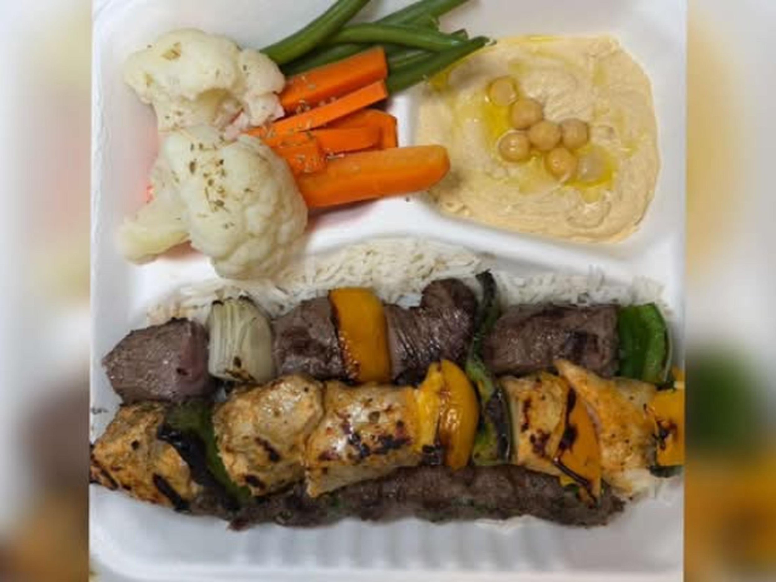 Assorted grilled meats, vegetables, mashed cauliflower, green beans, carrots, green peppers, and chickpeas served on a white plate.