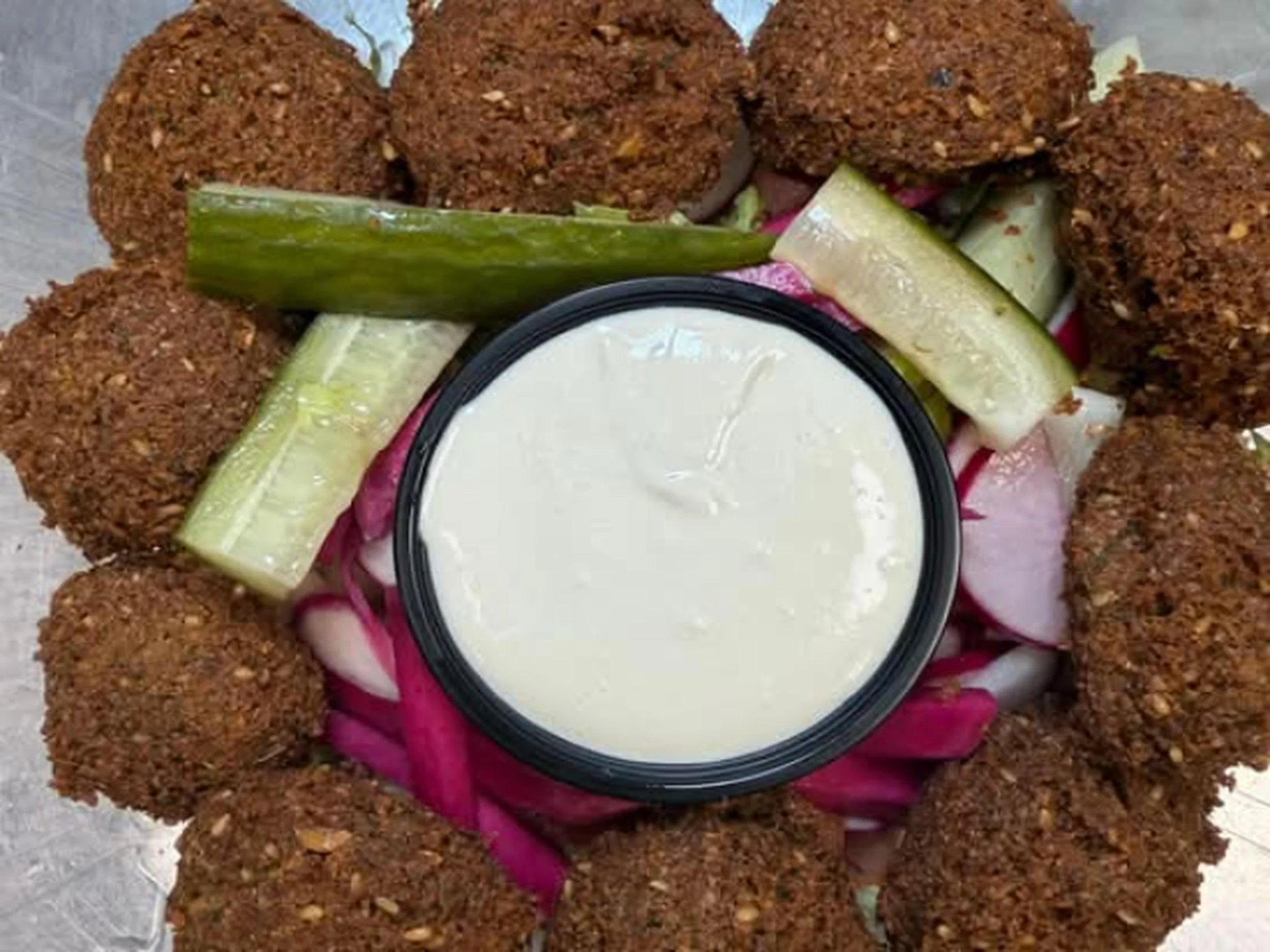 Fried croquettes arranged in a circle with pickle slices and a bowl of white dipping sauce in the center.