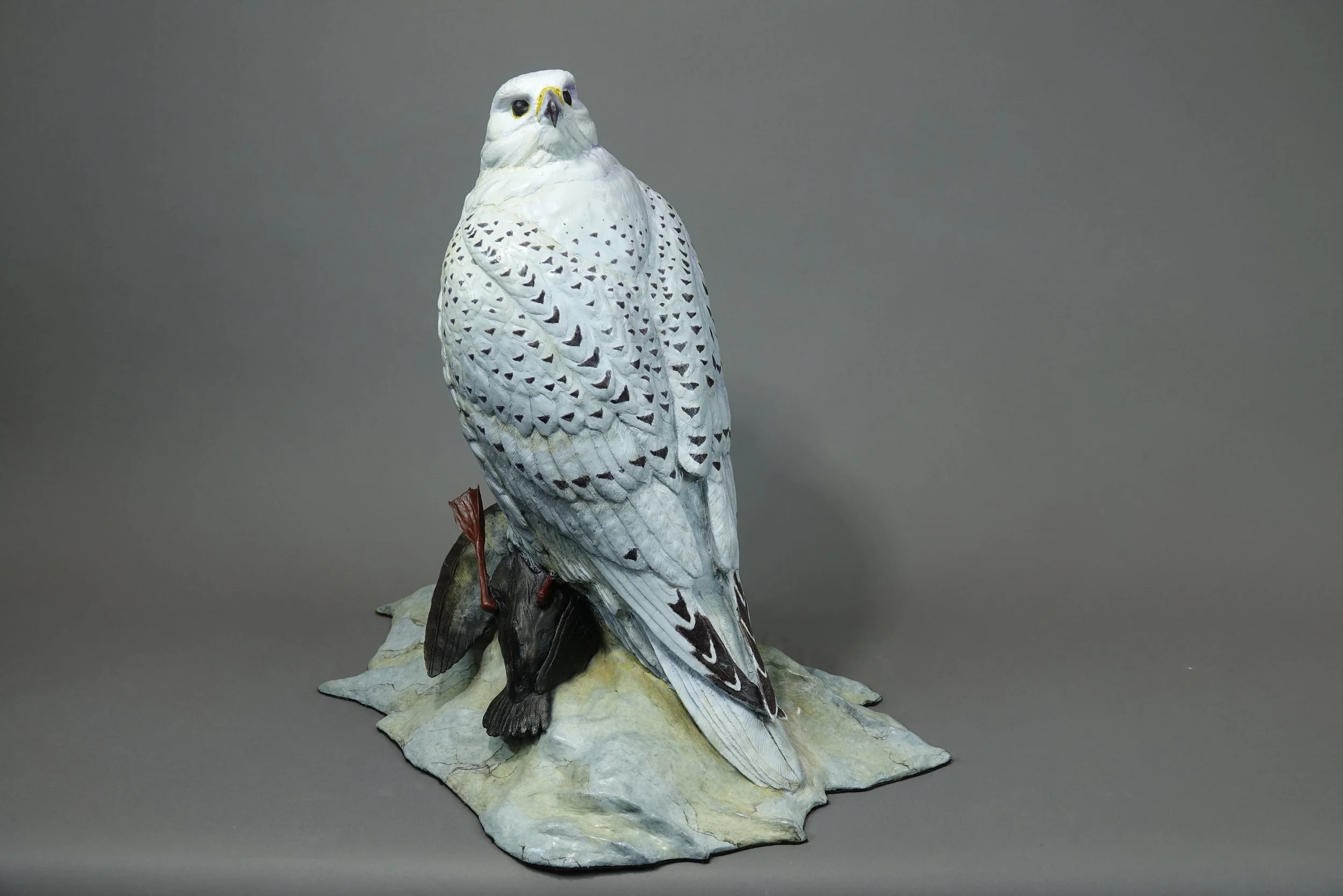 Taxidermy display of a snowy owl standing on a rock base.